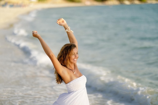 Young happy woman with raised arms having fun in summer day at the shore