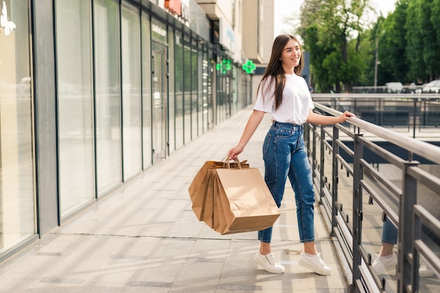 Young happy woman with shopping bags walking on store street.