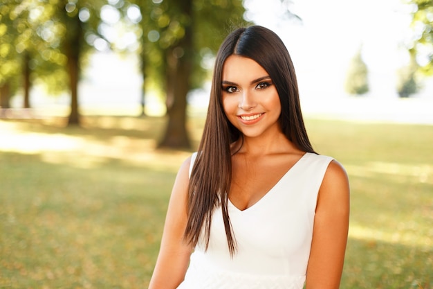 Young happy woman with a smile in a white dress on a summer day near trees