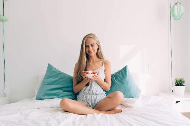 Young healthy beautiful blonde woman in the bed eating fruits