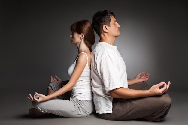 Young healthy couple in yoga position on dark background