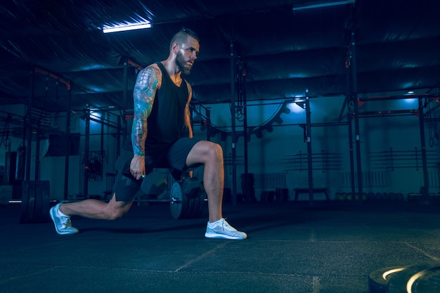 Young healthy man athlete doing exercise with the weights in the gym. Single male model training hard and practicing in squats. Concept of healthy lifestyle, sport, fitness, bodybuilding.