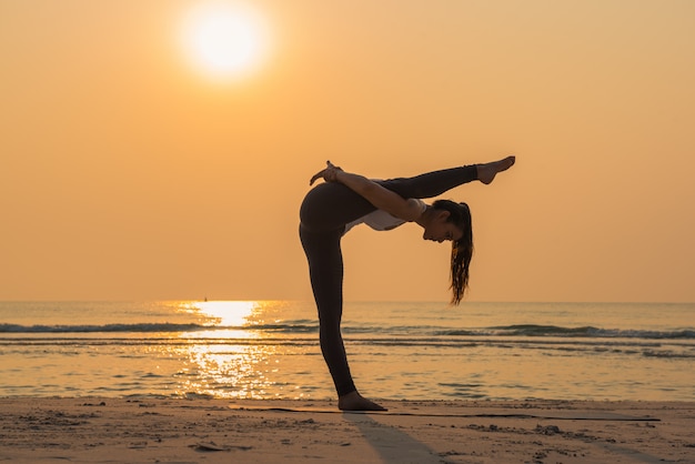 Young healthy Yoga woman practicing yoga pose on the beach at sunrise