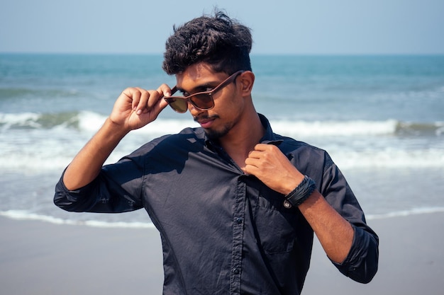 Young hindu stylish man posing with sunglasses active beach vacation on semmertime happy Goa India beach. sunscreen spf protection concept.