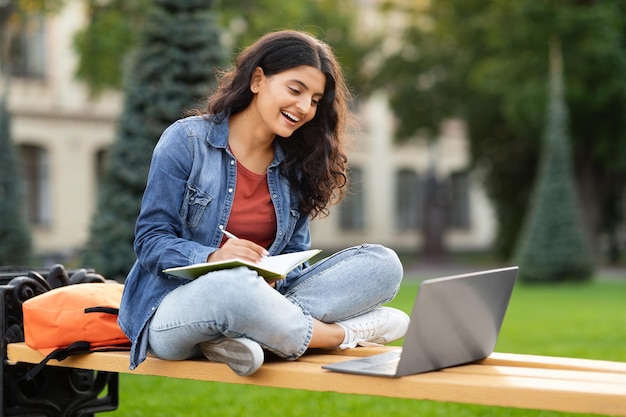 Young hindu woman student with laptop and notepad study outdoors