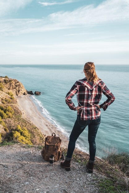 Young hip woman with a backpack explores the coast on a beautiful day. Concept of exploration and adventures