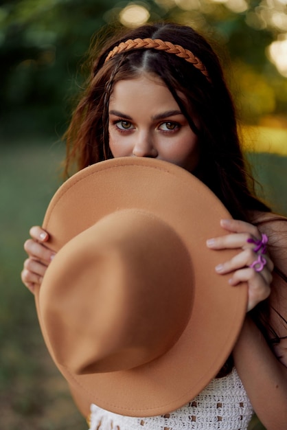 Young hippie woman holding a hat and smiling sincerely while looking at the camera in nature in the fall