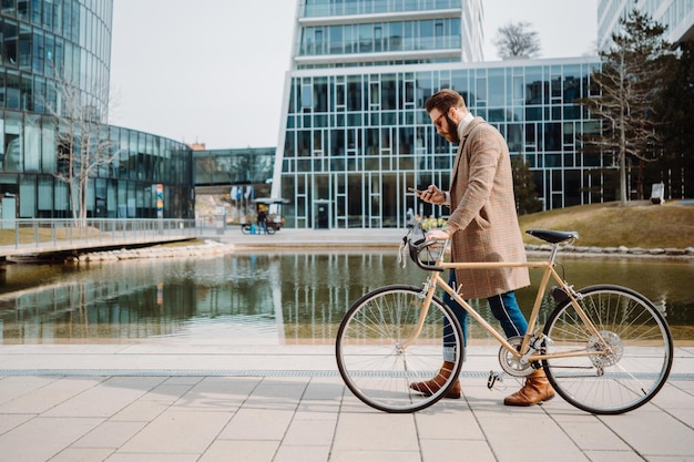 Young hipster businessman going to work with bicycle using smartphone eco friendly transport concept