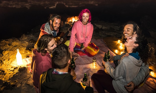 Young hipster friends having fun together at beach camping party by night