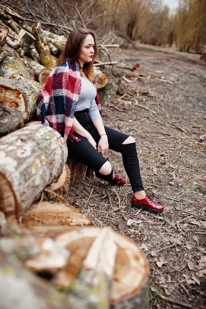 Young hipster girl wear on blanket against wooden stumps on wood.