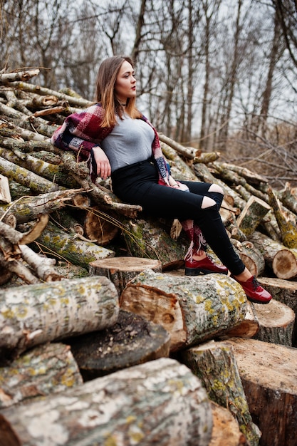 Young hipster girl wear on blanket against wooden stumps on wood.