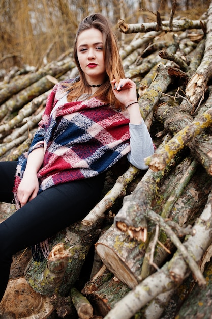 Young hipster girl wear on blanket against wooden stumps on wood.