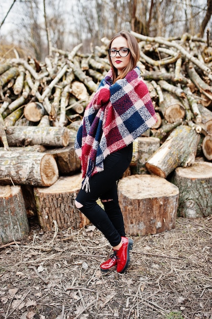 Young hipster girl wear on blanket and glasses against wooden stumps on wood.