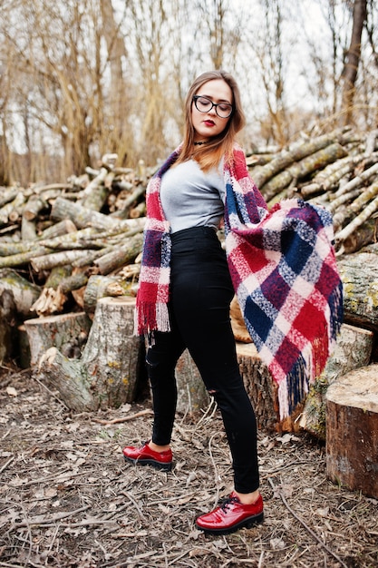 Young hipster girl wear on blanket and glasses against wooden stumps on wood.