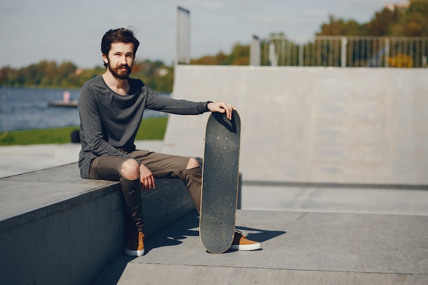 young hipster man sitting in a summer sunny park with a skateboard in his hands