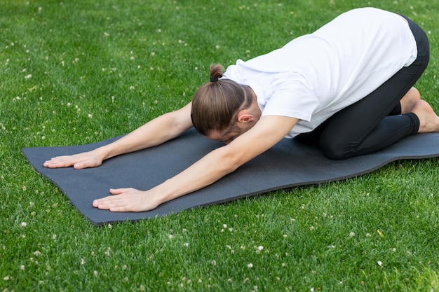 Young hipster unrecognizable man bended on the floor stretching on a yoga mat after exercising in the garden