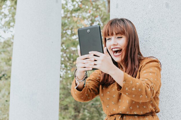 Young hipster woman on an autumnal dress laughs while making a video call on a tablet, hipster happy day, freedom and liberty concepts, ginger woman, social network style, copy space