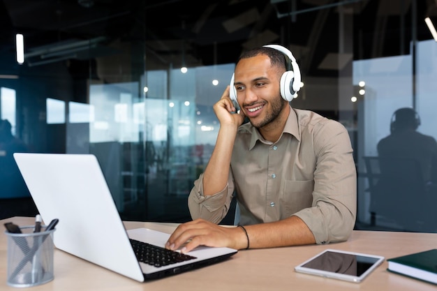 Young hispanic businessman in shirt working inside office using laptop at work man with headphones