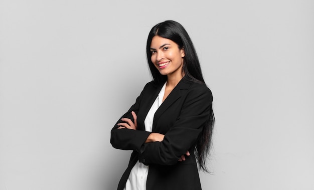 Young hispanic businesswoman smiling with crossed arms and a happy, confident, satisfied expression, lateral view