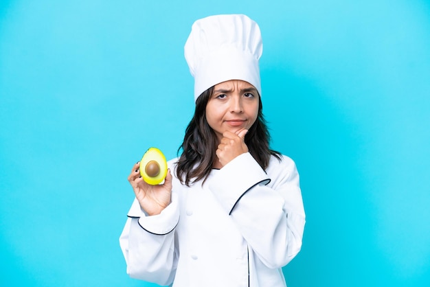 Young hispanic chef woman holding avocado isolated on blue background thinking