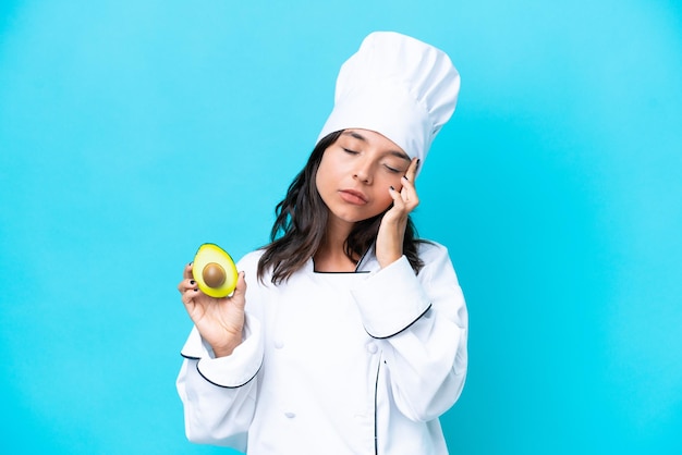 Young hispanic chef woman holding avocado isolated on blue background with headache