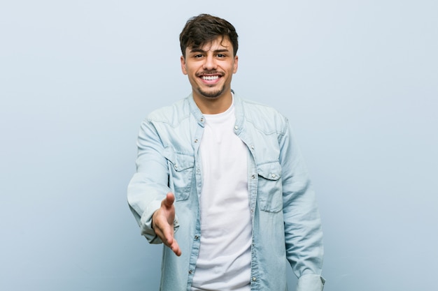 Young hispanic cool man stretching hand at camera in greeting gesture.