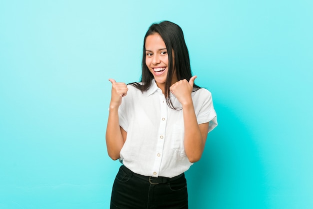 Young hispanic cool woman against a blue wall raising both thumbs up, smiling and confident.