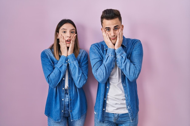 Young hispanic couple standing over pink background tired hands covering face depression and sadness upset and irritated for problem