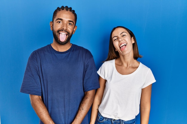 Young hispanic couple standing together sticking tongue out happy with funny expression emotion concept