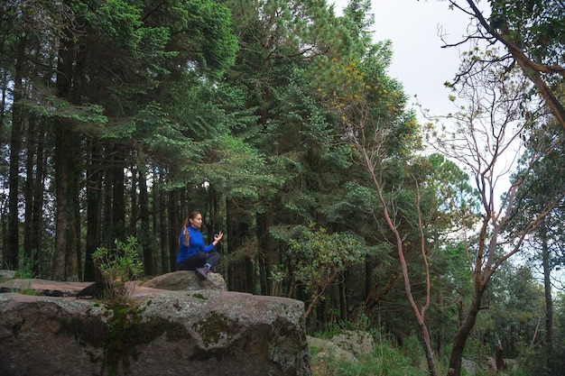 A young Hispanic female practicing yoga on a cliff in a forest