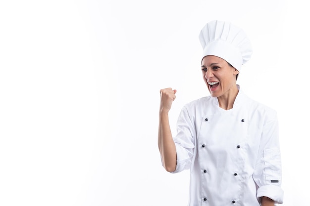 Young hispanic girl in cook uniform very happy and excited making winner gesture with arm raised smiling and shouting for success on white background with copy space