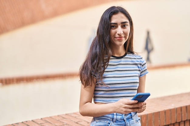 Young hispanic girl smiling confident using smartphone at street