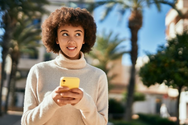 Young hispanic girl smiling happy using smartphone at the city