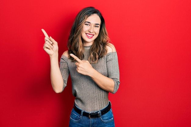 Young hispanic girl wearing casual clothes smiling and looking at the camera pointing with two hands and fingers to the side.