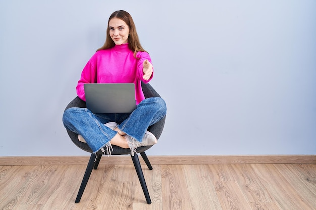 Young hispanic girl working using computer laptop smiling friendly offering handshake as greeting and welcoming. successful business.