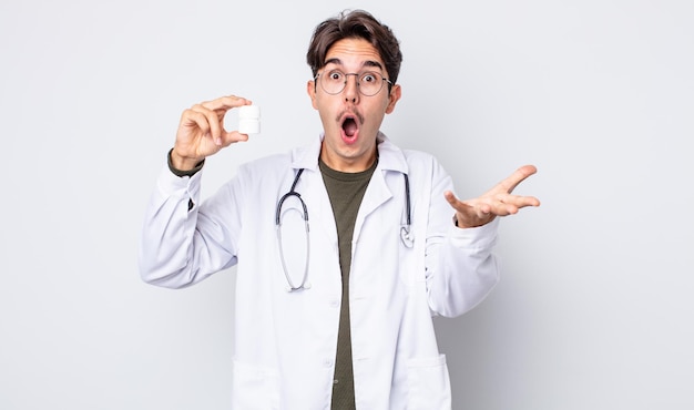 Young hispanic man amazed, shocked and astonished with an unbelievable surprise. physician with pills bottle concept