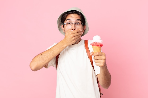 Young hispanic man covering mouth with hands with a shocked and holding an ice cream