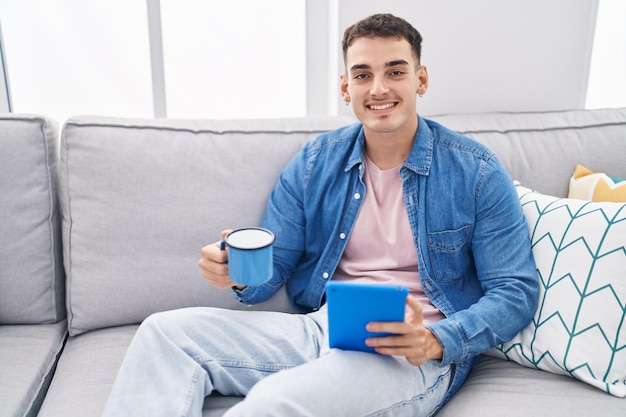 Young hispanic man drinking coffee using touchpad at home