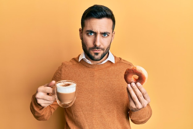 Photo young hispanic man eating doughnut and drinking coffee skeptic and nervous frowning upset because of problem negative person