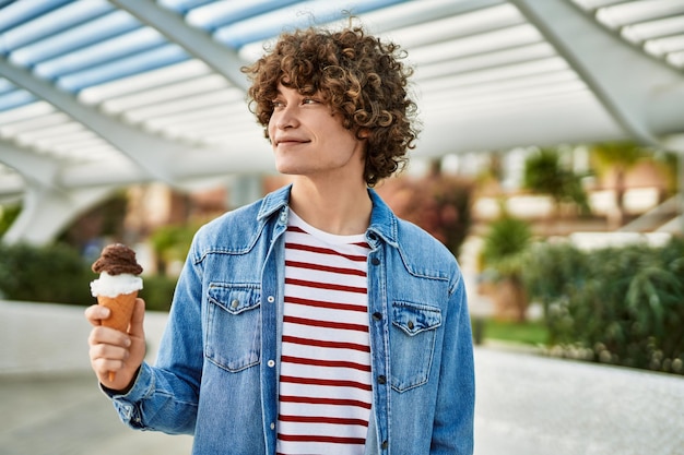 Young hispanic man eating ice cream cone at the city