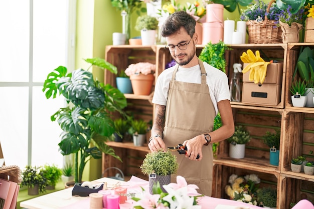 Young hispanic man florist cutting plant at flower shop