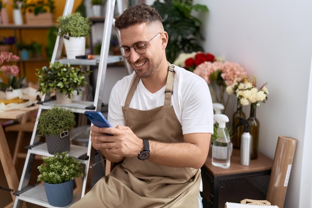 Young hispanic man florist smiling confident using smartphone at flower shop