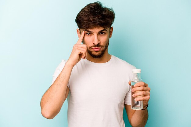 Young hispanic man holding a bottle of water isolated on white background pointing temple with finger thinking focused on a task