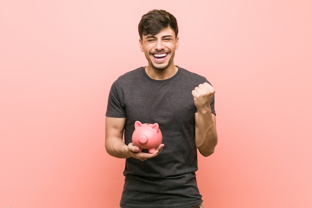 Young hispanic man holding piggy bank cheering carefree and excited. Victory concept.