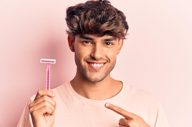 Young hispanic man holding razor smiling happy pointing with hand and finger