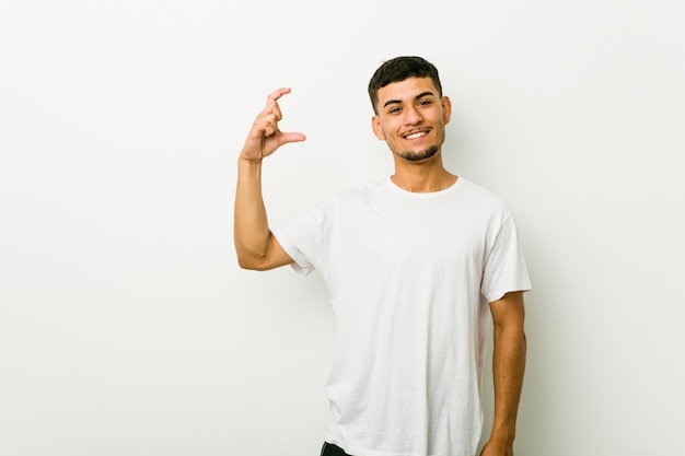 Young hispanic man holding something little with forefingers