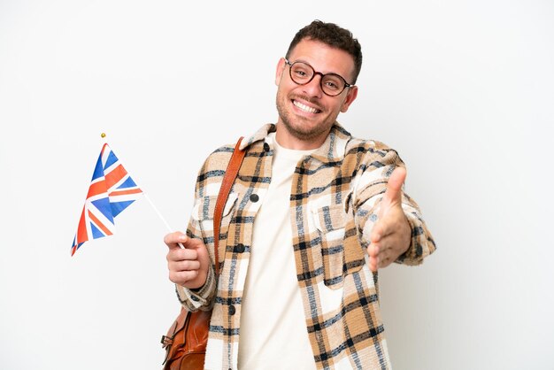 Young hispanic man holding an United Kingdom flag isolated on white background shaking hands for closing a good deal