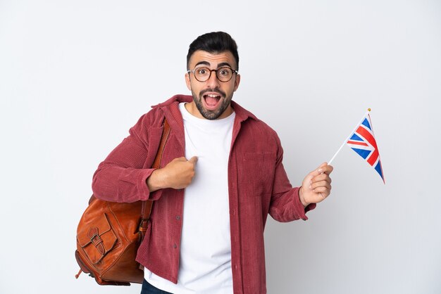 Young hispanic man holding an United Kingdom flag with surprise facial expression