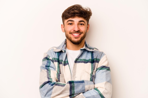 Young hispanic man isolated on white background who feels confident crossing arms with determination