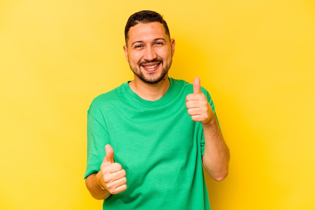 Young hispanic man isolated on yellow background raising both thumbs up smiling and confident